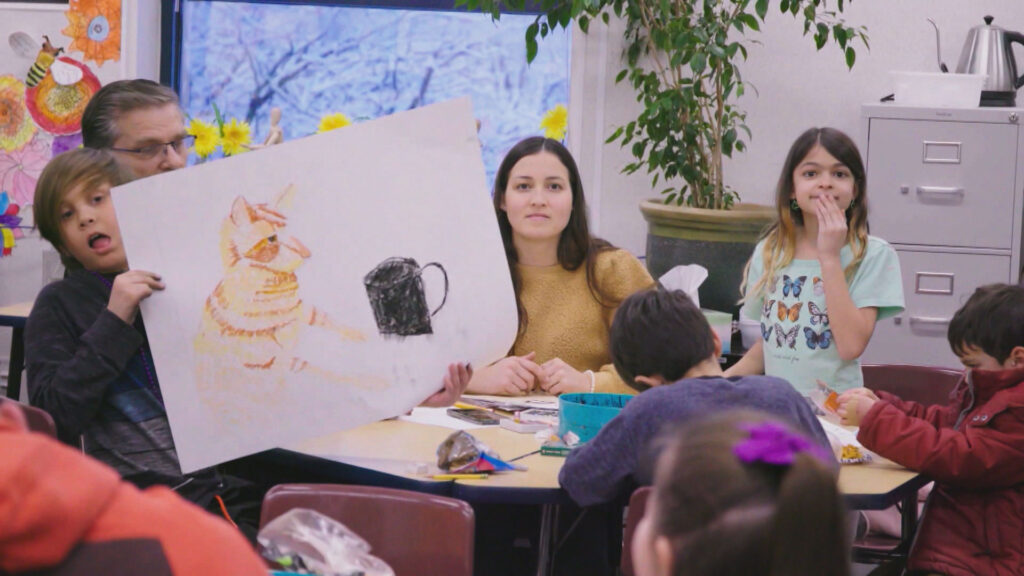A group of children are sitting around a table with a picture of a cat.