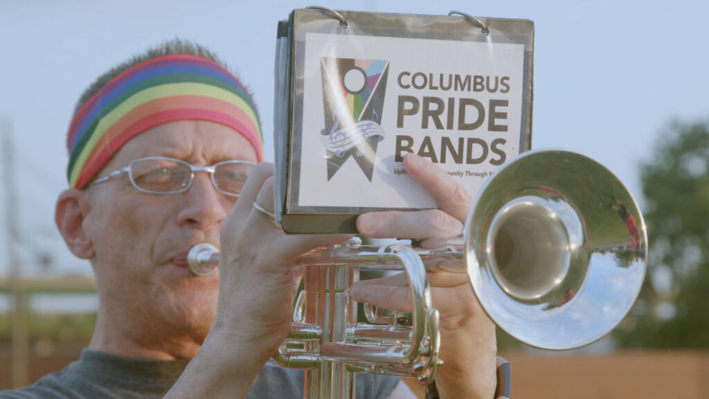 A man playing a trumpet in front of a sign that says columbus pride bands.