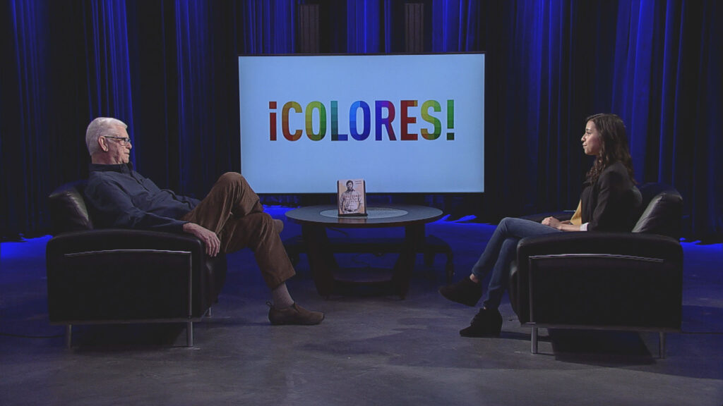 Two people sitting in chairs in front of a tv with the word icolores.