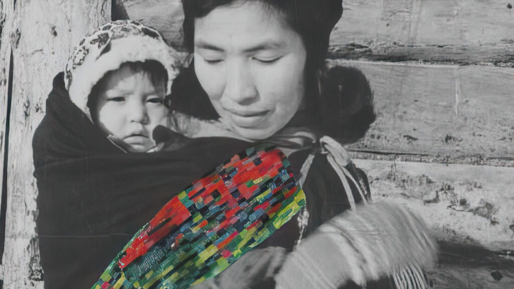 A woman carrying a child on her back, with a colorful woven fabric sling, standing beside a wooden structure.