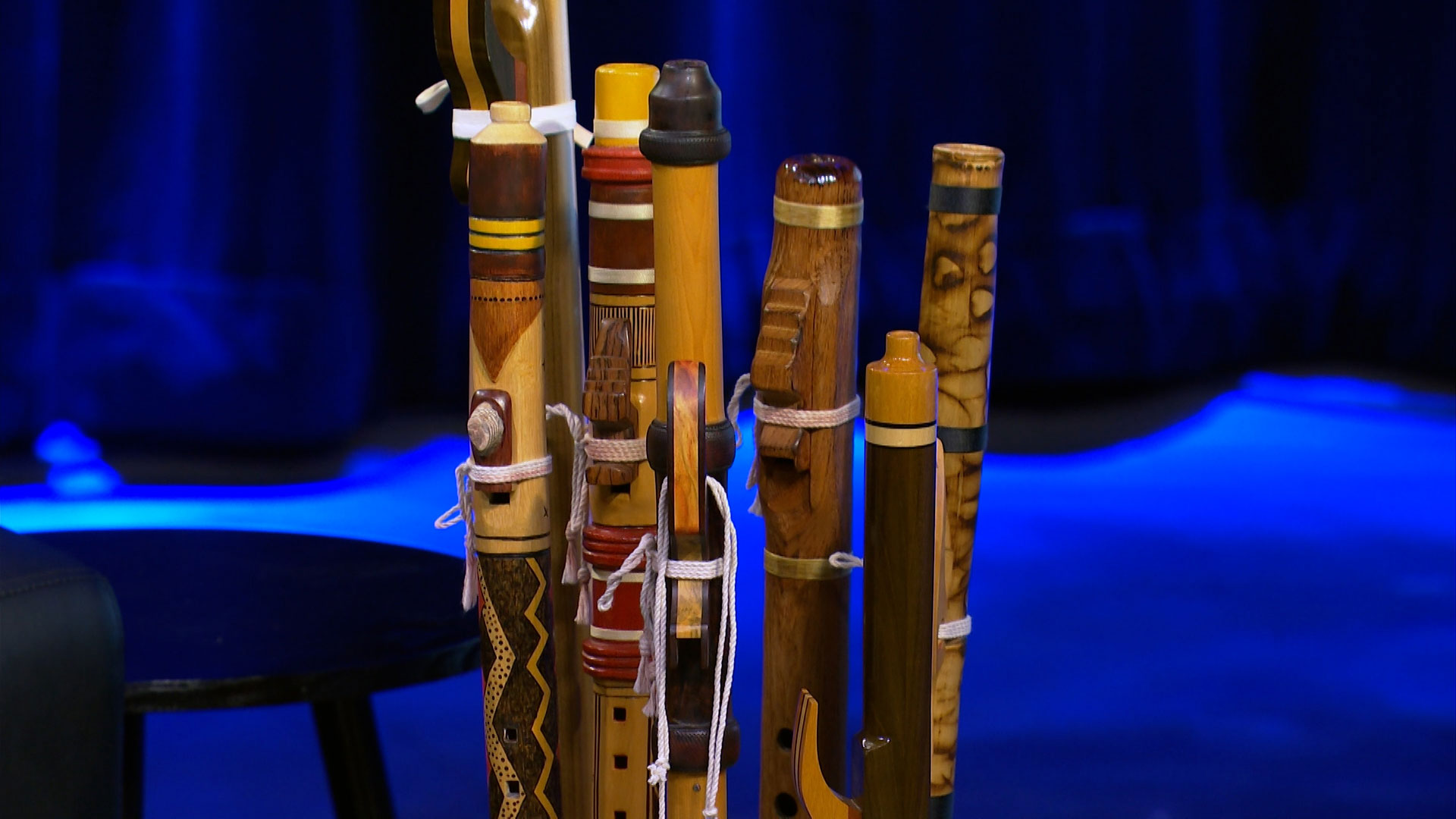A group of wooden flutes with various carvings and decorations are tied together and displayed upright against a dark blue background.