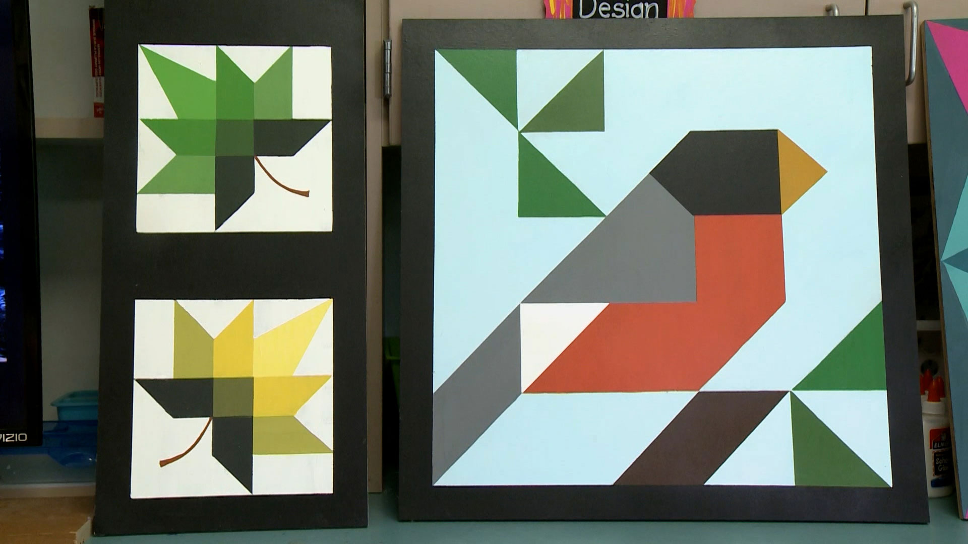 Two geometric artworks: one with two stylized leaves in green and yellow, and one with a bird in a blocky, abstract design using green, black, orange, gray, and white shapes.
