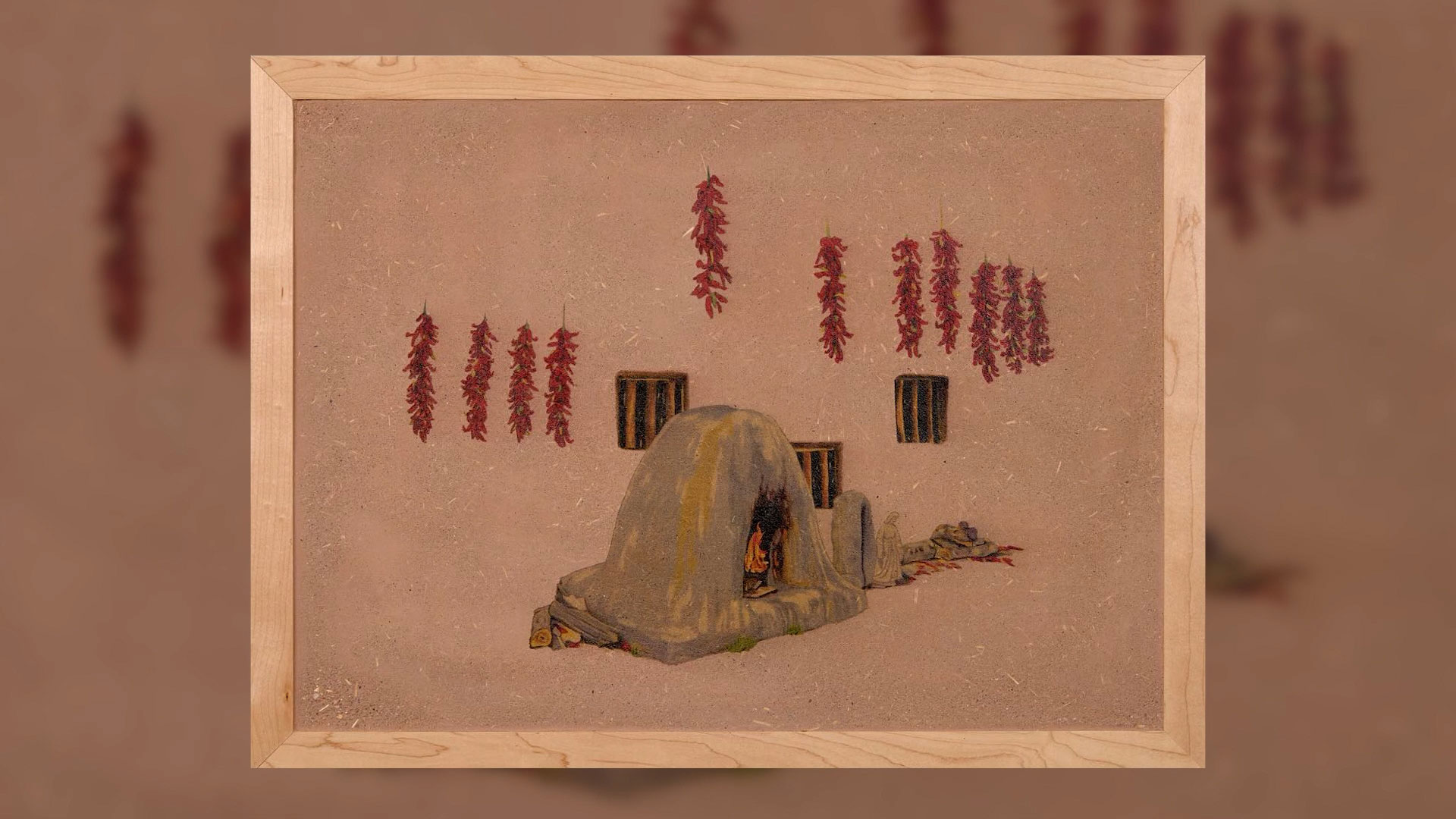 A painting of an adobe oven with red chili ristras hanging on a beige wall, framed in light wood.