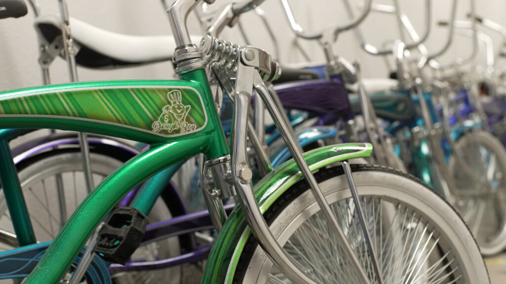 Row of colorful vintage bicycles with chrome handlebars and fenders, featuring a green bike with decorative stripes and a logo in the foreground.