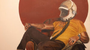 A person wearing a vintage-style astronaut helmet sits on a chair, dressed in casual clothes, with a red circular background.