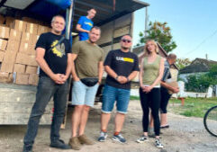 A group of people stands in front of an open truck loaded with boxes. Two individuals are inside the truck, while others are standing on the ground.