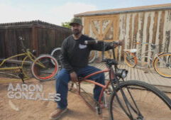 A man sits on a custom-built bicycle in a yard with two other bicycles and a wooden shed in the background. The name "Aaron Gonzales" is displayed on the image.