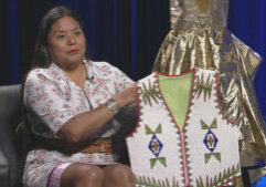 A woman sits in front of a mannequin wearing a vest.