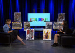 Two people sit in armchairs on a studio set with artwork displayed between them and a screen behind them reading "¡COLORES!" in colorful letters.