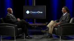 Two men sitting in chairs talking on a television.