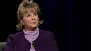 A woman in a purple jacket sitting in a chair.