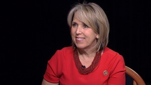 A woman in a red shirt is sitting in a chair.