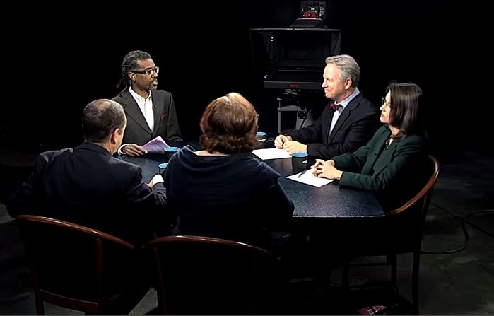 A group of people sitting around a table in front of a camera.