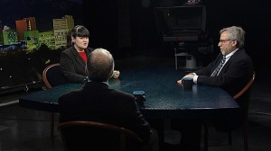 Three people sitting at a table in front of a television screen.