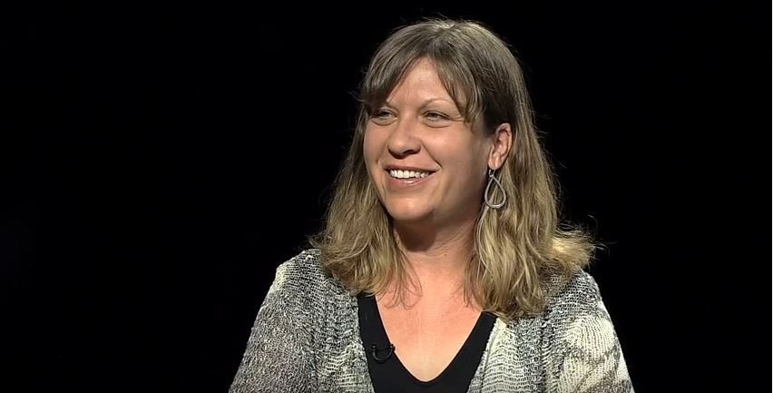 A woman is smiling in front of a black background.