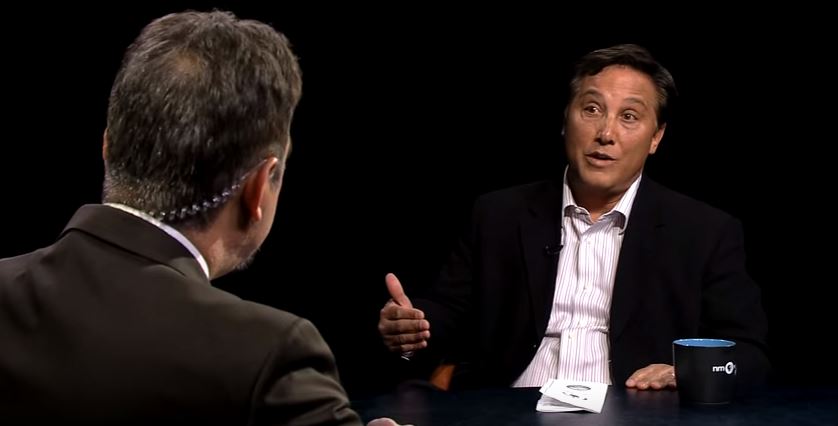 Two men sitting at a table talking to each other.