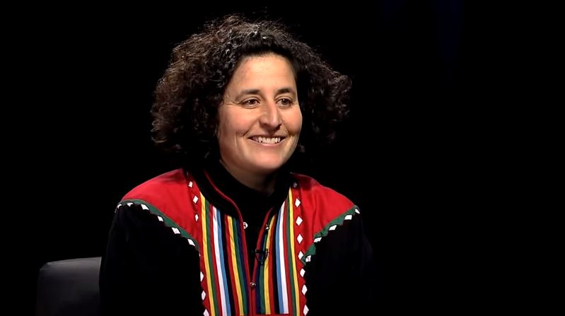 A woman with curly hair sitting on a chair.