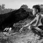 A man squatting next to a log.