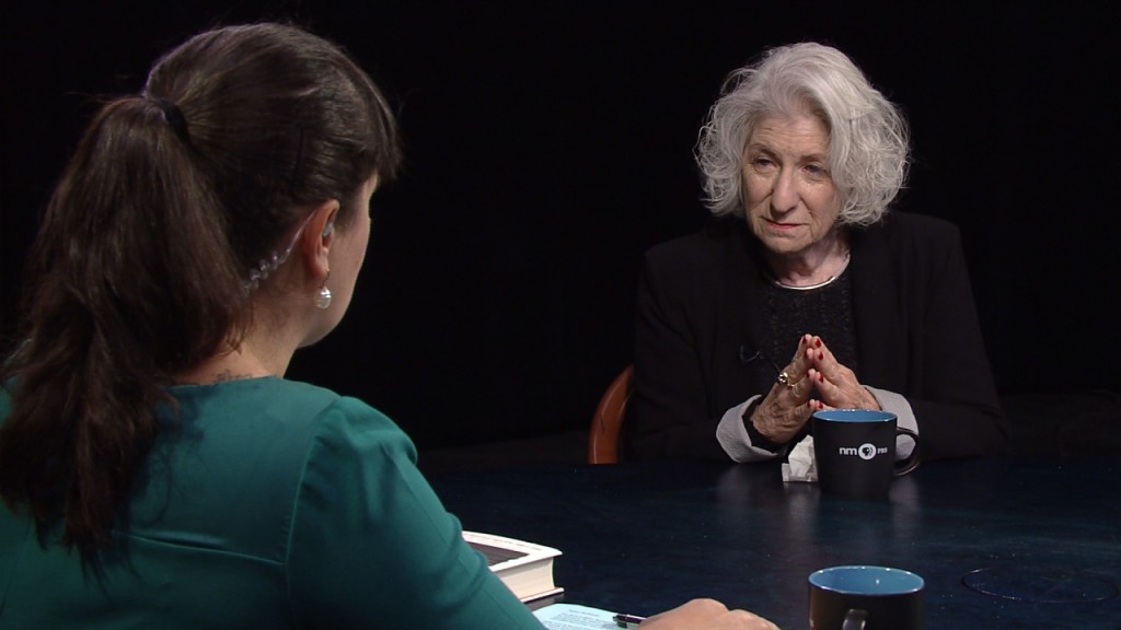 An older woman sitting at a table with a cup of coffee.