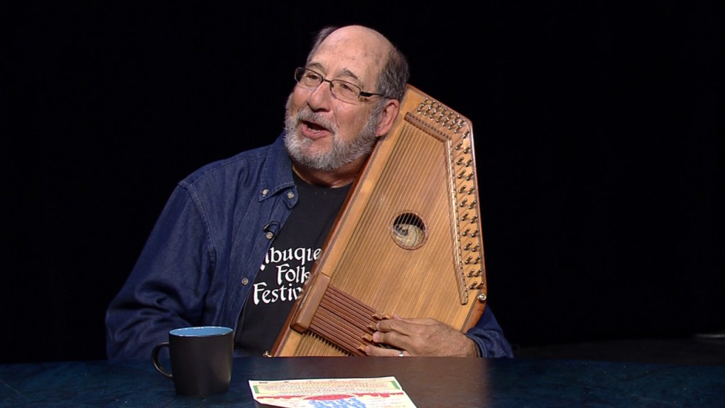 A man sitting at a table holding a wooden harp.