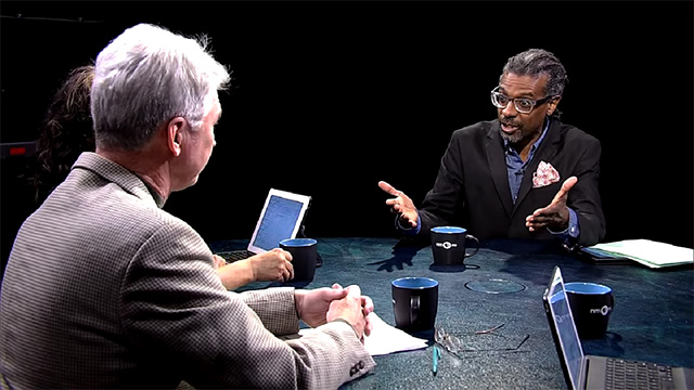 Two men sitting at a table talking to each other.