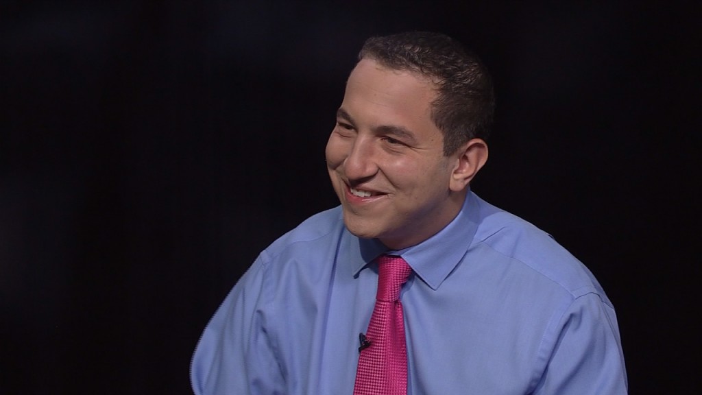 A man in a blue shirt and pink tie is smiling.