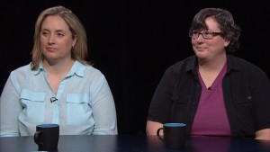 Two women sitting at a table with coffee mugs.