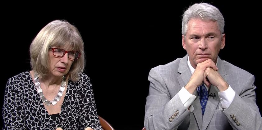 A man and a woman sitting in front of a black background.