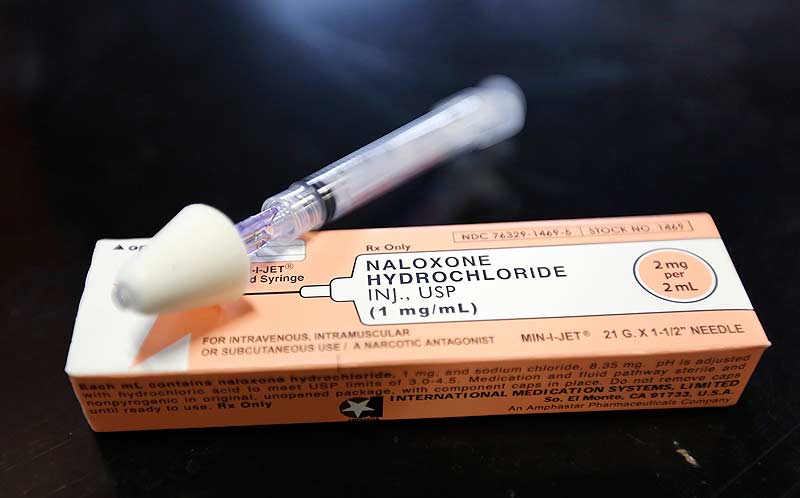 A syringe of naloxone sits next to a box.
