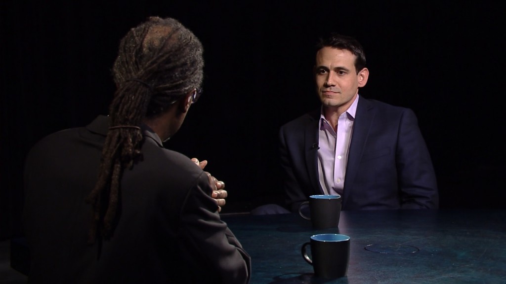 Two men sitting at a table talking to each other.