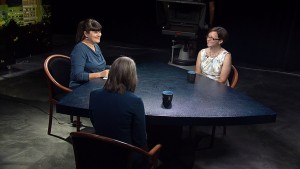 Three women sitting at a table in front of a camera.