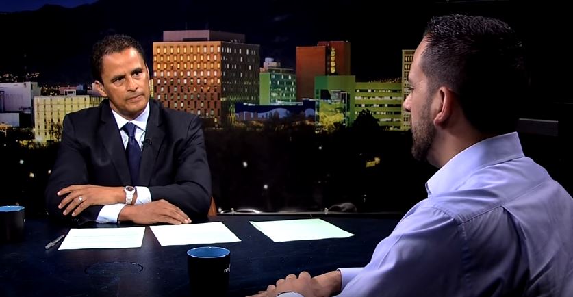 Two men sitting at a table in front of a city.