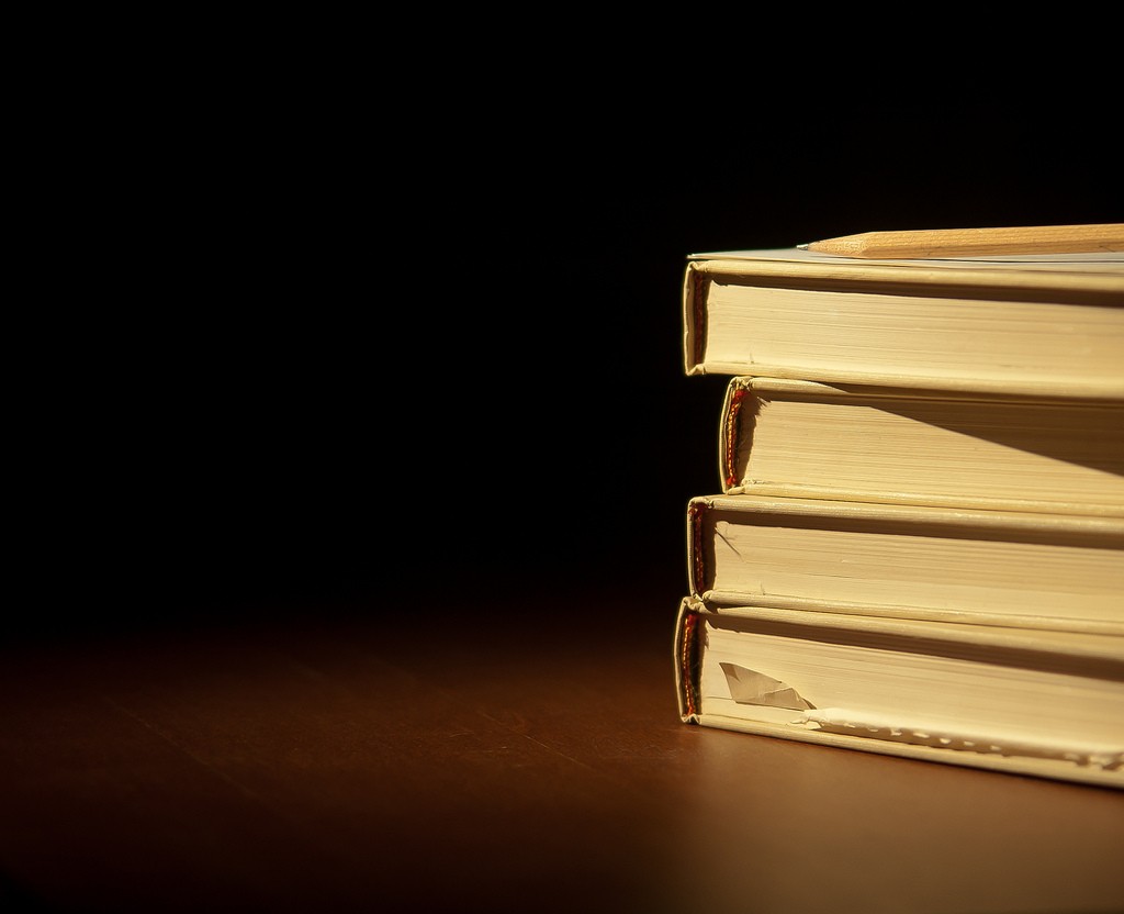 A stack of books with a pencil on top.