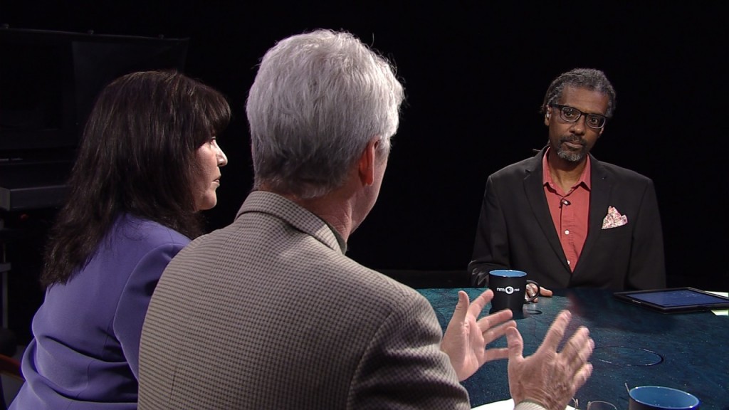 Three people sitting at a table talking to each other.