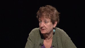 A woman with short hair wearing a green shirt and earrings.