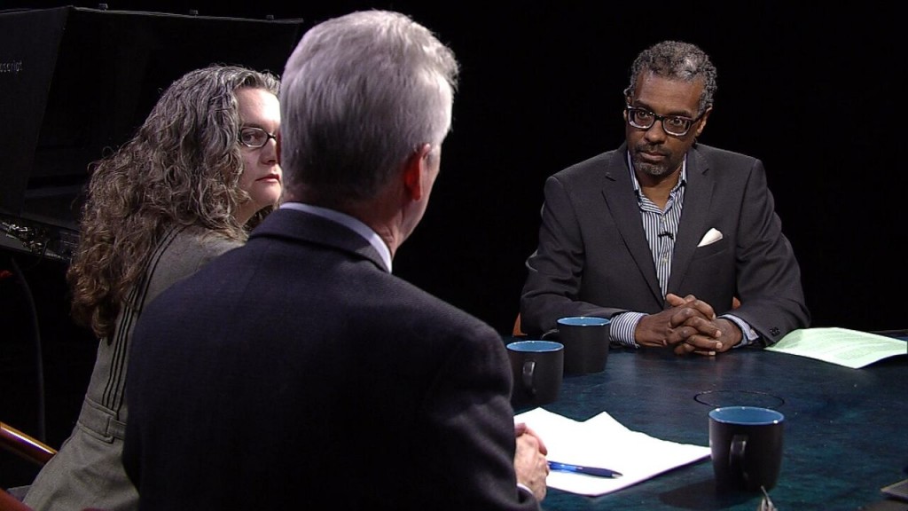 Three people sitting at a table talking to each other.