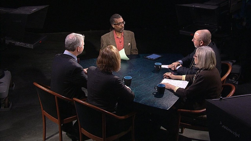 A group of people sitting around a table in front of a camera.