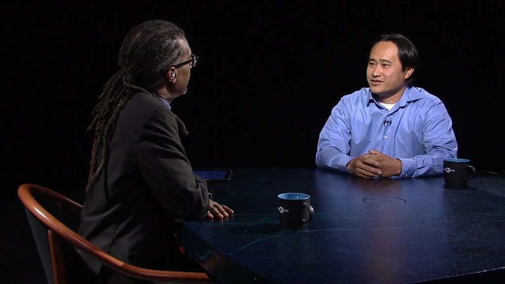 Two men sitting at a table talking to each other.