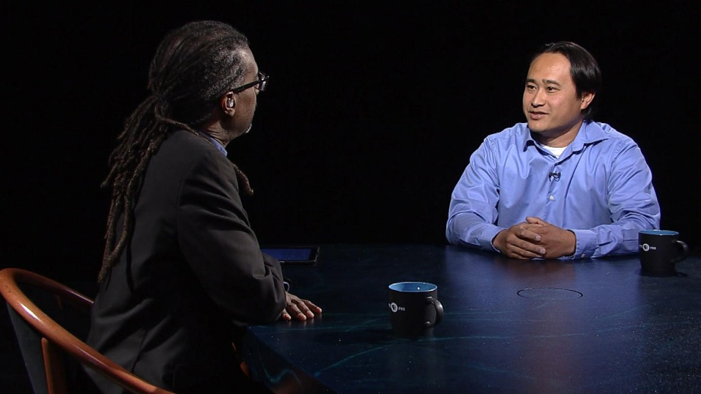 Two men sitting at a table talking to each other.