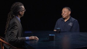 Two men sitting at a table talking to each other.