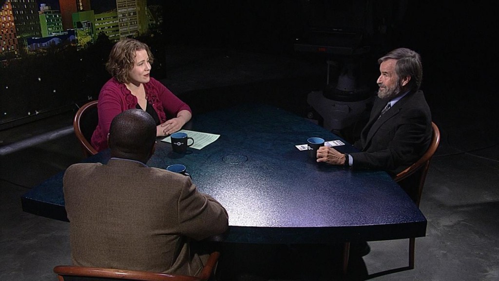 Three people sitting at a table in front of a television.