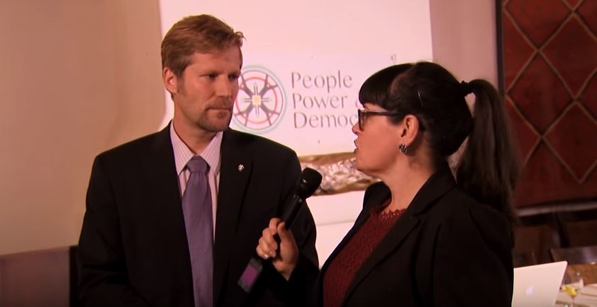 A woman in a suit and tie talking to a man in a suit.