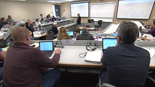 A group of people sitting at desks in a conference room.