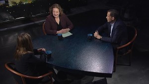 Three people sitting at a table in front of a television.