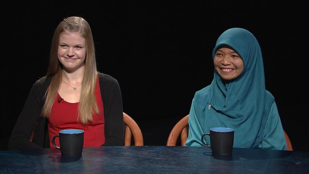 Two muslim women sitting at a table with mugs.