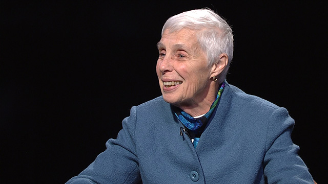 A woman in a blue jacket is sitting at a table.