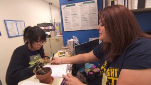 A woman sitting at a desk with a plant in front of her.