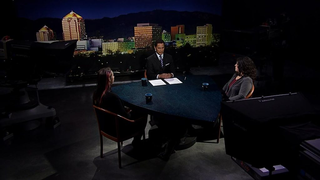 Two people sitting at a table in front of a camera.