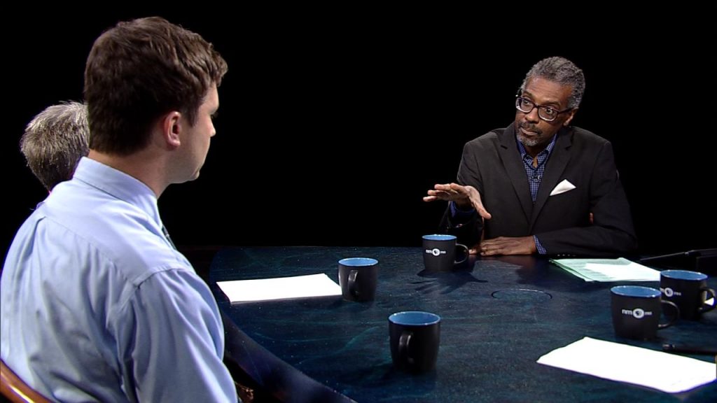 Three men sitting at a table talking to each other.