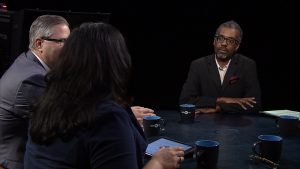 Three people sitting at a table talking to each other.